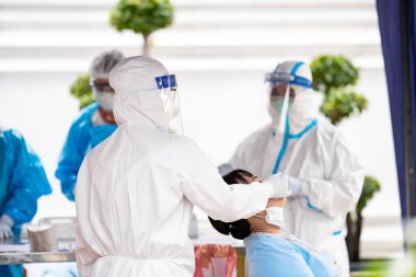 A nurse in white gown and face shield is taking nasal swab sample for patient.