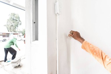 Home PaintBush in professional worker man hand is painting interior in the corner of the wall.