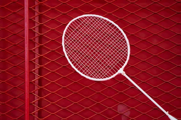 one badminton racket is hung on red grill by a cable tie for display in exhibition sports event