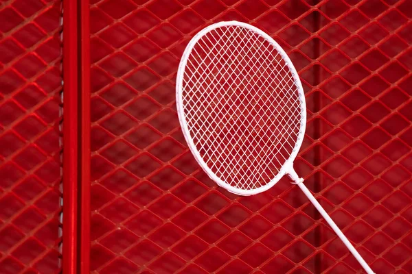 one badminton racket is hung on red grill by a cable tie for display in exhibition sports event