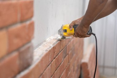 Kapalı işçi el testeresi makinesini tutuyor ve duvar kurulumu için tuğla köpük levha kesiyor.