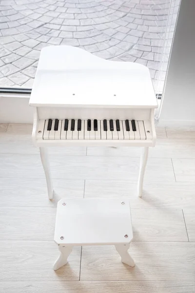 White piano big toy for kid in front of mirror in white room.
