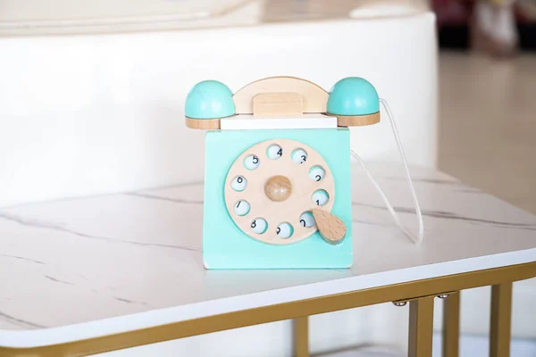 An antique blue turquoise white rotary home phone toy made of wood rests on a white marble patterned shelf for kids learning and play.