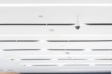 White Closed circuit television CCTV is hung on a white ceiling beside the air vents.