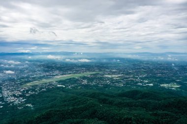Top view of mountain in Chiang Mai City, Thailand. White cloud and dust is above of the mountain while cities can be seen far away.