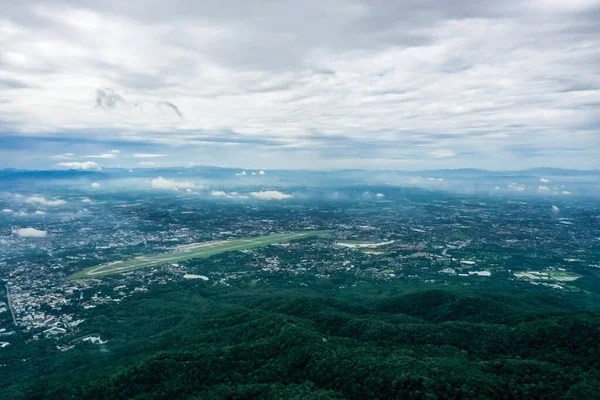 Top view of mountain in Chiang Mai City, Thailand. White cloud and dust is above of the mountain while cities can be seen far away.