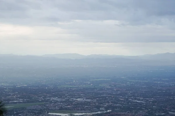 Top view of mountain in Chiang Mai City, Thailand. White cloud and dust is above of the mountain while cities can be seen far away.