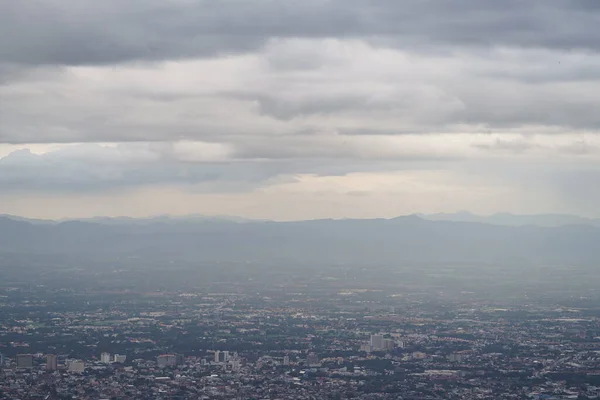 Top view of mountain in Chiang Mai City, Thailand. White cloud and dust is above of the mountain while cities can be seen far away.