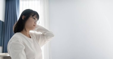 Gözlüklü genç Asyalı kadın elini kulağına kaldırıyor Mutlu ve gevşeme hissi açık mavi arka planda.