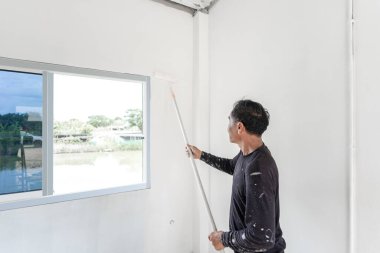 professional worker man is rolling and painting interior white wall.