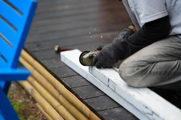 Construction worker blacksmith cuts the whitewashed steel into smaller pieces for DIY project on a brown wooden floor.