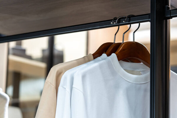 Shirts hang in a walking closet wiht beige and white T shirt on it.