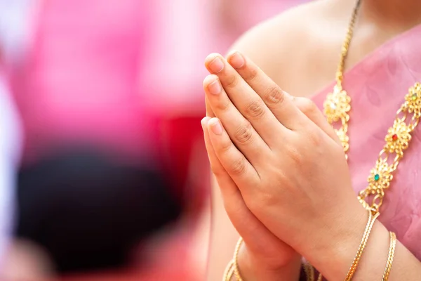 A Lady clasps her hands in front of her chest to pray. She wears
