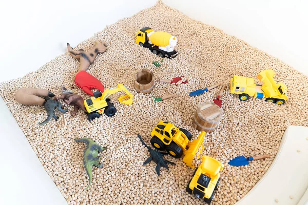 yellow construction toy vehicles and Dinosaurs Toys are placed in kids playground filled with wooden cubes around it