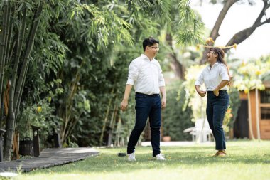 Asyalı bir adam ve bir kadın düğün öncesi bir fotoğraf çekiyorlar. Bir kadın adamın omzunu tutuyor ve bahçedeki adamı kucaklıyor..