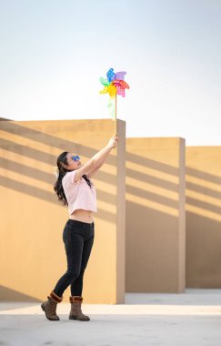 Asyalı kadın, gün batımında çatıda renkli gökkuşağı renginde Windmill Toy oynar ve ilan verir..