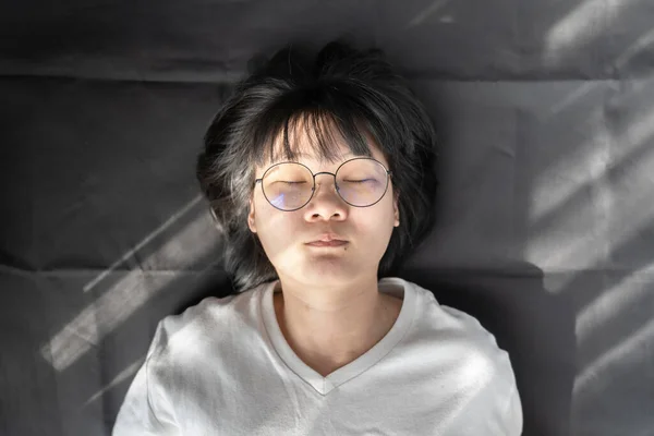 漂亮的短头发眼镜亚洲女人躺在黑色皱巴巴的背景上 窗上有灯光 — 图库照片