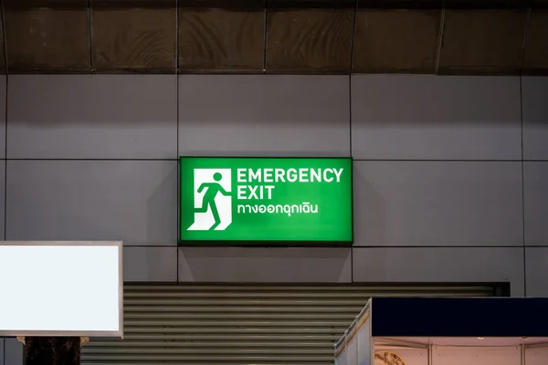 Large Emergency exit sign green light box is placed on the wall of exhibition hall. Thai Letter is Thai Language on the green light box mean EXIT.
