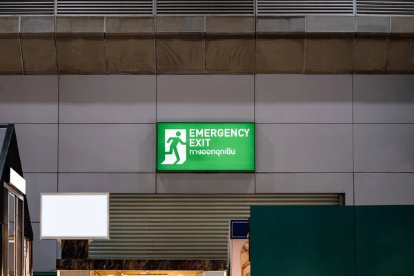 Large Emergency exit sign green light box is placed on the wall of exhibition hall. Thai Letter is Thai Language on the green light box mean EXIT.