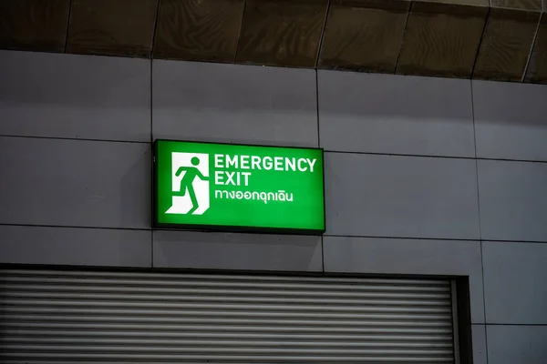 Large Emergency exit sign green light box is placed on the wall of exhibition hall. Thai Letter is Thai Language on the green light box mean EXIT.