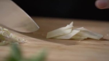 Galangal, ahşap bir tahtanın üzerinde kesilip küçük parçalara bölünüyor ve profesyonel bir şef tarafından mutfak bıçağıyla dilimleniyor..