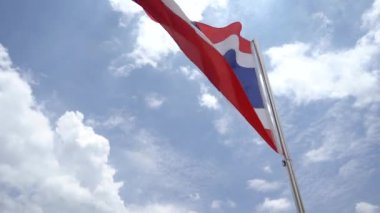 Tayland 'ın ulusal bayrağı mavi gökyüzünde rüzgar ve bulutlarla dalgalanıyor. Kırmızı, beyaz, mavi, beyaz ve kırmızı yatay çizgilerden oluşur..