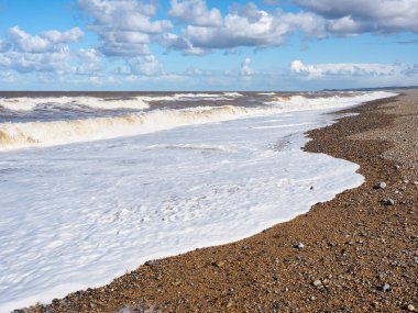 Dalgalar mavi gökyüzü ve beyaz bulutların altında sahile çarpar, Blakeney Point, Norfolk