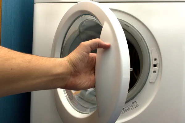 Mann öffnet Waschmaschine im Badezimmer lizenzfreie Stockbilder