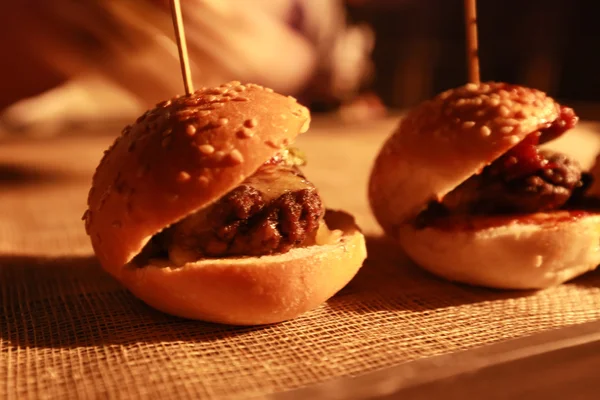 Hamburger schuifregelaars op een rustieke houten snijplank. — Stockfoto