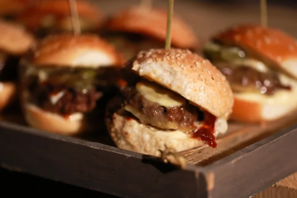 Hamburger schuifregelaars op een rustieke houten snijplank. — Stockfoto