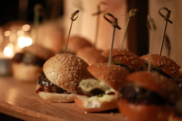 Hamburger schuifregelaars op een rustieke houten snijplank. — Stockfoto