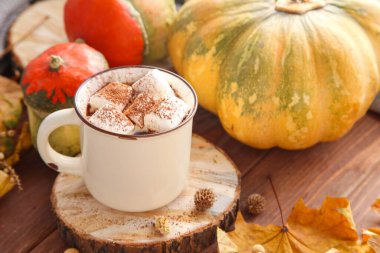 Sıcak bir sonbahar sabahı kabaklı bir fincan kakao ve ahşap arka planda sonbahar yapraklarıyla.