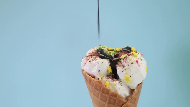 Cono con helado sobre fondo azul se vierte con chocolate — Vídeos de Stock