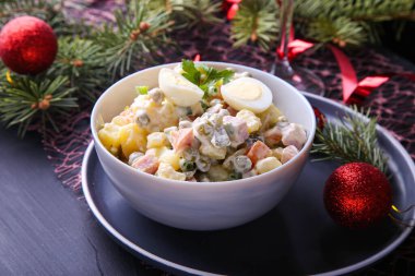 Geleneksel Rus salatası Olivier Noel ve yeni yıl için karanlık bir arka planda. Firavun ağacı dalları, kırmızı kurdeleler ve toplar. Görüntüyü kapat