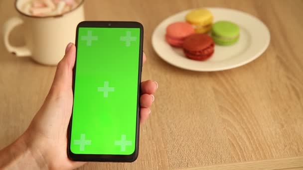 Chica mira a un teléfono inteligente con una pantalla verde en el café. Teléfono con pantalla verde y clave de croma para el espacio de copia. Chromakey Mockup con marcadores de seguimiento. — Vídeo de stock