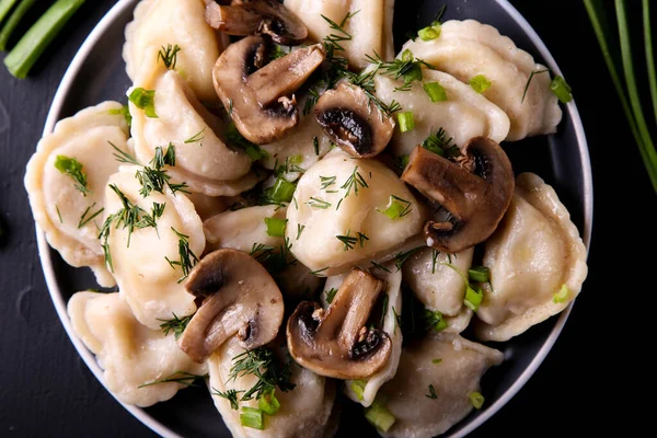 Dumplings with mushrooms on a black background with onions, garlic and eggs. Vareniki is a dish of Slavic cuisine