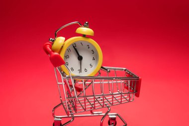 Alışveriş zamanı. Kırmızı arka planda alışveriş sepetindeki sarı alarm saati. Boşluğu kopyala. 