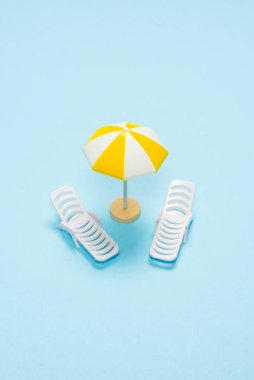 Seyahat konsepti. Güneş şezlongu, mavi arka planda sarı şemsiye. Boşluğu kopyala. 