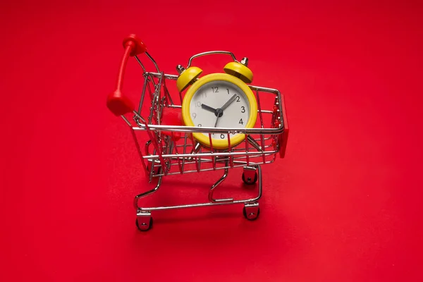 Bevásárlás Sárga Ébresztőóra Bevásárlókosárban Piros Háttérrel Fénymásolási Hely — Stock Fotó