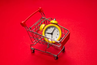 Alışveriş zamanı. Kırmızı arka planda alışveriş sepetindeki sarı alarm saati. Boşluğu kopyala. 
