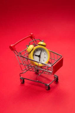 Alışveriş zamanı. Kırmızı arka planda alışveriş sepetindeki sarı alarm saati. Boşluğu kopyala. 