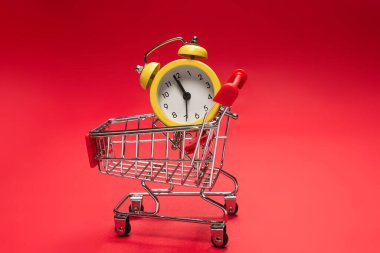 Alışveriş zamanı. Kırmızı arka planda alışveriş sepetindeki sarı alarm saati. Boşluğu kopyala. 