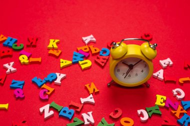 Kırmızı arkaplanda rastgele renkli alfabe ve sarı alarm saati, renkli harfler. Okula gitme vakti. Çalışma zamanı. Eğitim zamanı..