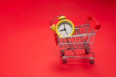Alışveriş zamanı. Kırmızı arka planda alışveriş sepetindeki sarı alarm saati. Boşluğu kopyala. 