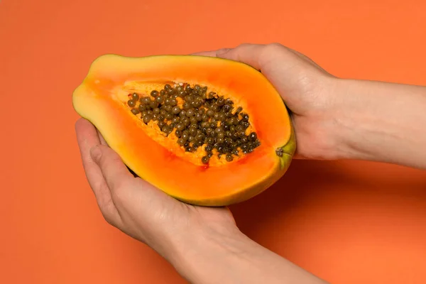 Papaya fruit on a orange background in woman hands. Tropical fruit. Half papaya.