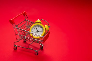 Alışveriş zamanı. Kırmızı arka planda alışveriş sepetindeki sarı alarm saati. Boşluğu kopyala. 