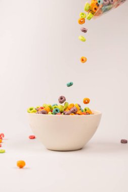 Sabah kahvaltısı için renkli mısır gevreği kutusu. Mısır gevrekleri beyaz kaseye düşüyor. Hareket. Kopyalama alanı.