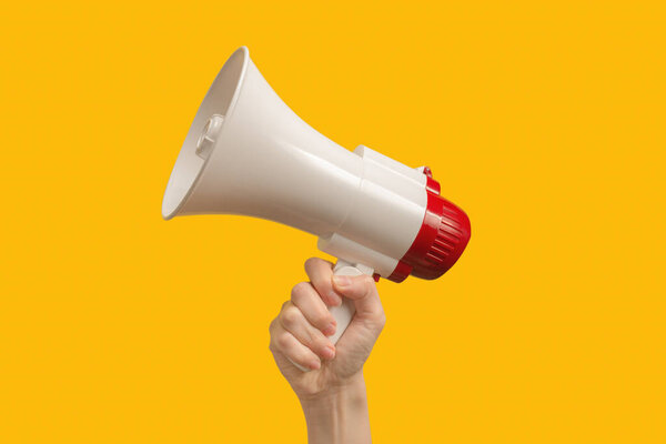 Мегафон в женских руках на жёлтом фоне. Копирование пространства. 