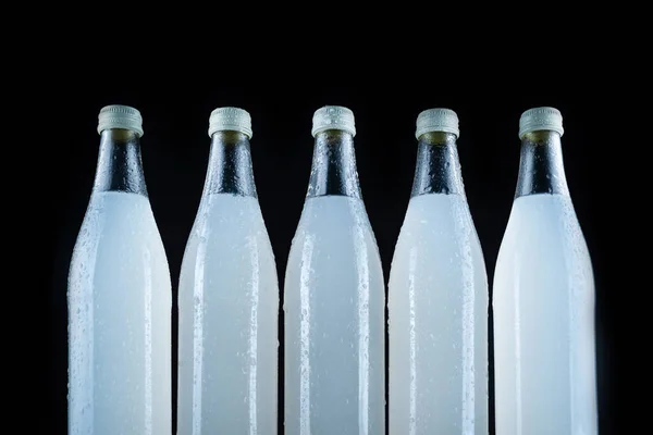 A white bottle with a soda drink on ice on a black background.