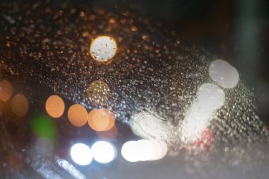 Yağmur damlaları ve ışıklarla bulanık arkaplan.